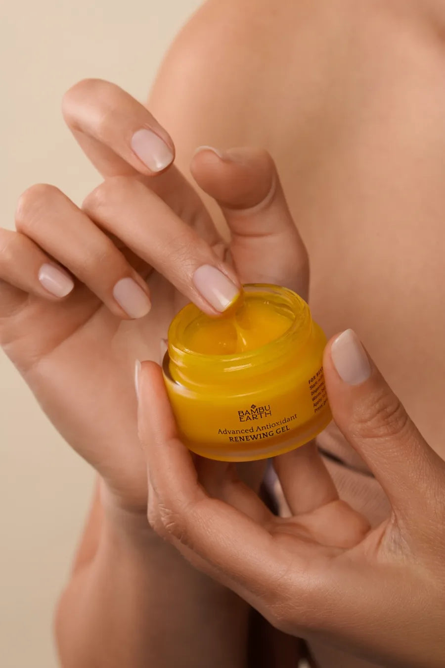 Hands lifting a pea-sized amount of Renewing Gel from the open jar