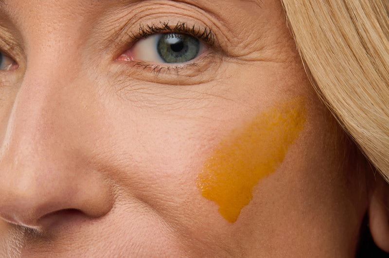 Close-up of a woman's cheek and eye area with a swatch of the golden gel on her cheekbone.