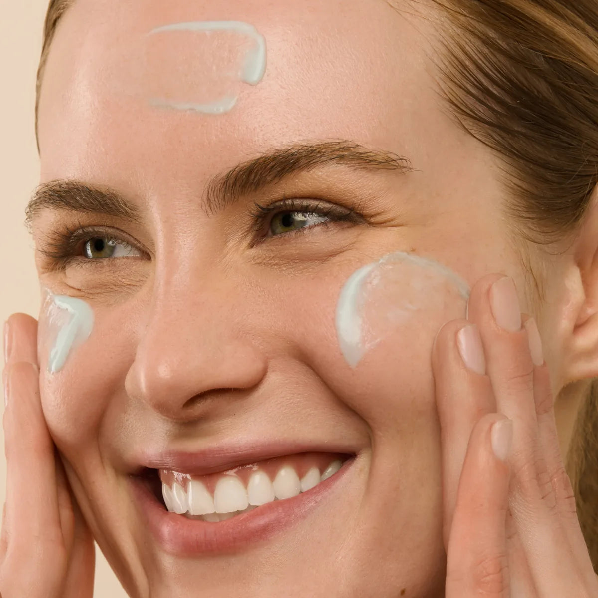 Smiling person pressing the serum into their cheeks and forehead