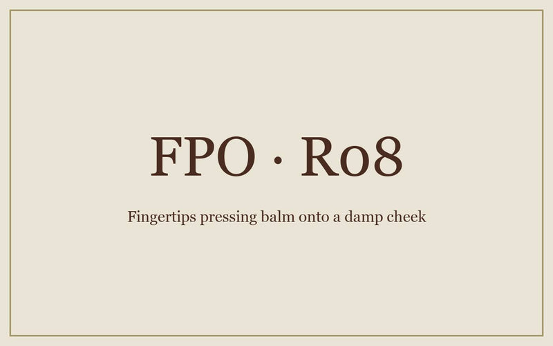 FPO: fingertips pressing balm onto a damp cheek, foundation waiting on the counter.