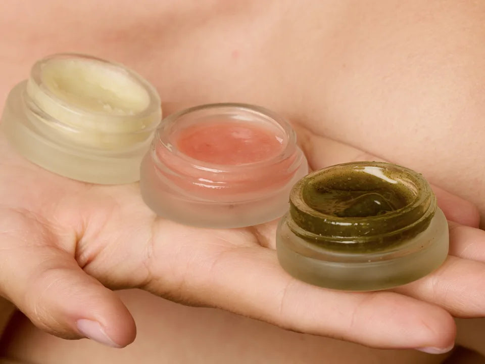 Three open mini jars held in a hand, showing shea butter, papaya, and bambu willow textures
